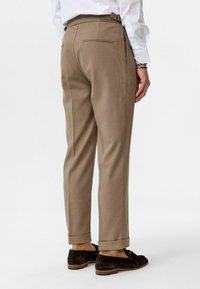 Beige gestreepte broek met een tapered fit, met een achterzak en opgerolde boorden. Gemaakt van lichte stof, met een gladde textuur.