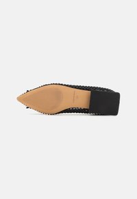 Zapato negro de punta afilada con parte superior trenzada y tacón cuadrado. Presenta una suela marrón claro con estrías y la marca visible en el interior del zapato.
