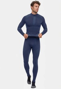 Navy long-sleeve athletic top with a high collar and textured details, paired with fitted navy leggings. Material appears moisture-wicking.