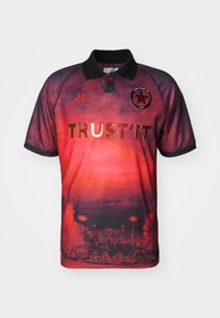 Maglia corta rossa e nera con colletto, un logo a stella e il testo "TRUST IT". Il design include un gradiente e illustrazioni dettagliate nella parte inferiore.