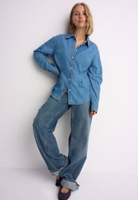 Lichtblauw denimoverhemd met knopen, lange mouwen en een losse pasvorm, gecombineerd met wijde blauwe jeans met opgerolde zomen.