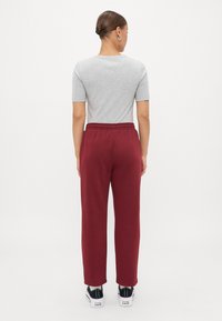 Maglietta grigia a maniche corte abbinata a pantaloni della tuta bordeaux con cinturino elastico, completata da sneakers nere e bianche.