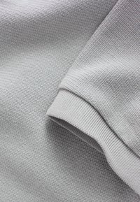 Hellgrauer, strukturierter Stoff mit einem gewebten Muster und einem gerippten Bündchen-Detail. Robustes Material mit einer weichen Oberfläche.