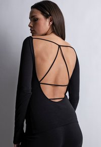 Haut noir à manches longues présentant un dos décolleté avec plusieurs fines bretelles formant un motif géométrique. Tissu doux avec une coupe ajustée.