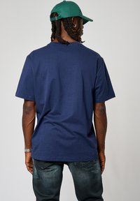 T-shirt en coton bleu marine à manches courtes, col rond et coupe décontractée. Le dos est sans ornement et le tissu a une texture lisse.