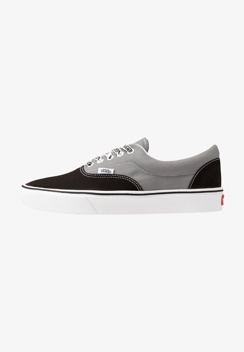 Baskets basses Vans en toile noire et grise avec lacets blancs, semelle en caoutchouc blanche, et étiquettes logo Vans sur le côté et la languette.