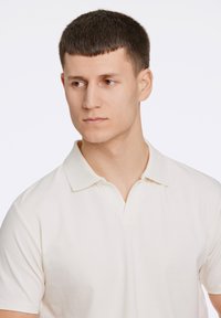 Pikétröja i off-white bomull med klassisk krage, korta ärmar och en subtil struktur. Har en knappslå med två knappar.