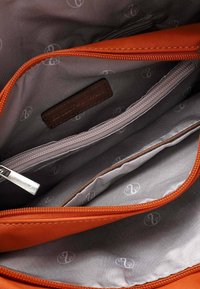 Oranges Reißverschlussbeutel mit grauem Innenfutter, mit einem Lederetikett und mehreren Fächern, darunter eine Reißverschlusstasche.