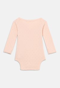 Lyserød babybody med lange ærmer og små hjerteformede hulmønstre samt bølgekant på krave og ærmekanter.