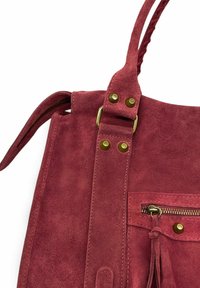 Sac à main en daim de couleur rose profond, avec une bandoulière tressée, des ferrures en laiton et une poche zippée ornée d'un détail à pompon.