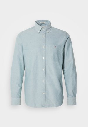 Camisa abotonada de color azul claro con mangas largas, un bolsillo en el pecho y un pequeño detalle de logo. Fabricada con una tela suave y texturizada.