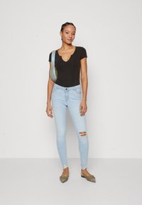 Fekete, bordás, rövid ujjú body, világoskék, szakadt skinny farmerekkel és barna lapos cipőkkel. A modellen világoszöld, vállra akasztható táska van.