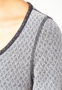 Gray patterned textile showcasing a subtle diamond design, edge-stitched neckline in black, featuring a soft, textured fabric.