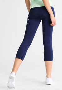 Granatowe legginsy capri z elastycznego materiału o dopasowanym kroju. Posiadają dyskretny, biały detal logo po lewej stronie.