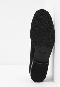 Tmavě modrá semišová bota s kulatou gumovou podrážkou, která má dvanáct kruhových výstupků pro lepší přilnavost. Na podrážce je značka "Gabor" a nápis "Vyrobeno v Portugalsku".