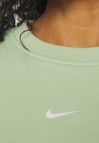 Camiseta Nike verde claro con cuello redondo acanalado y un pequeño logo de swoosh blanco en el pecho. Textura de tela de algodón suave.