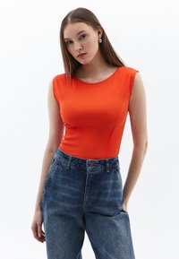 Top senza maniche aderente in morbido tessuto a costine arancione brillante, abbinato a jeans in denim blu scuro a vita alta con chiusura a bottoni e tasche.