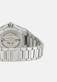 Montre en acier inoxydable avec un boîtier octagonal, fond détaillé affichant le mouvement, et un bracelet à maillons rectangulaires.