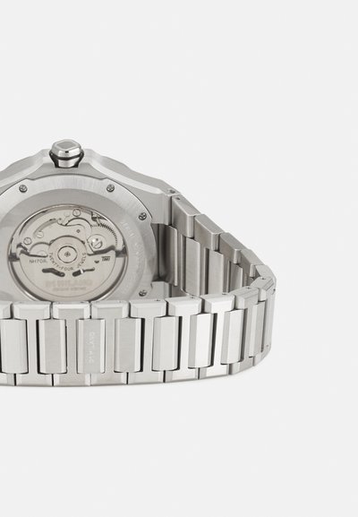 Ura iz nerjavečega jekla z osmokotno ohišjem, podrobnim zadnjim delom, ki prikazuje mehanizem, ter povezanim zapestnim trakom z pravokotnimi povezavami.