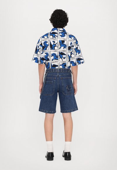 Cămașă cu mâneci scurte, cu un model de cai alb și albastru, asociată cu șorturi din denim albastru, de lungime medie, cu buzunare și bucle pentru curea. Pantofi negri și șosete albe.