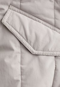 Tissu matelassé gris clair avec un motif cousu diagonal et un rabat rectangulaire proéminent aux bords nets et avec une légère brillance.