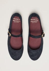 Un par de zapatos Mary Jane negros con correas de hebilla dorada y plantillas burdeos de la marca "Woman by Fred Martin Made in Spain" sobre un fondo claro.