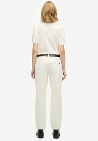 Camiseta blanca combinada con pantalones blancos de talle alto, con un cinturón negro. El conjunto tiene un ajuste casual y un diseño minimalista. Botas negras completan el look.