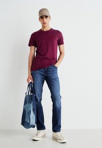Bordo īsām piedurknēm T-krekls, zilo džinsu bikses, bēša cepure un krēmkrāsas sneakers. Tur zilu un gaiši zilu rakstainu soma.