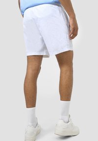 Vita shorts i lätt material med elastiskt midjeband och sidofickor, tillsammans med vita sneakers och randiga vita strumpor.