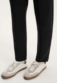 Čierne zúžené nohavice skombinované s nízkoprofilovými teniskami s mixom bieleho, béžového a hnedého materiálu, šnurované a textúrované.