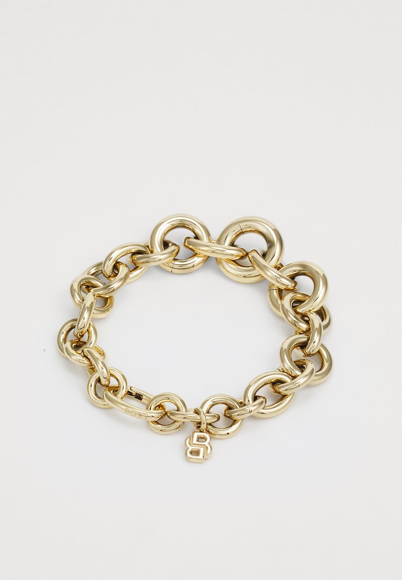Bracciale in metallo dorato con catena di anelli ovali interconnessi e finitura lucida, con un piccolo ciondolo che mostra una lettera "B" stilizzata.