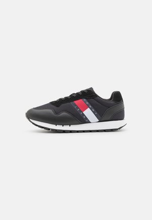 Scarpa da ginnastica nera con una combinazione di pelle liscia e tessuto testurizzato. Strisce rosse, bianche e blu navy sui lati. Suola bianca.