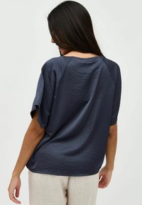 Blusa blu navy a maniche corte con texture stropicciata, scollo rotondo e maniche raglan, abbinata a pantaloni chiari e texturizzati.