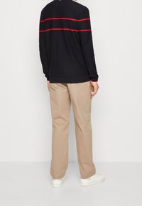 Pull à manches longues bleu marine avec des rayures rouges horizontales, associé à un pantalon beige à jambes droites et des baskets blanches, vu de dos.