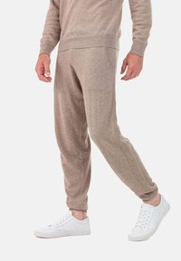Joggers en tissu doux couleur beige avec taille et poignets côtelés, dotés de poches latérales et d'une coupe fuselée, associés à des baskets blanches.