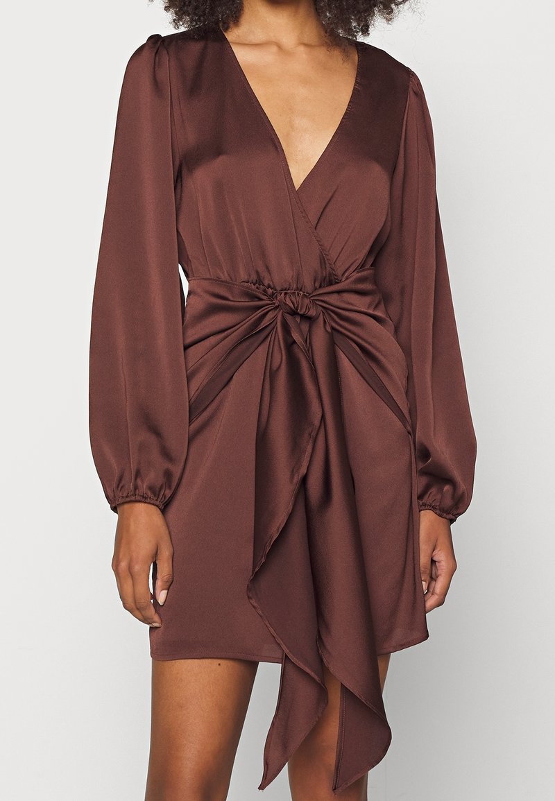Brun satinklänning med djup V-ringning, långa puffärmar och samlad midja. Har en vriden detalj fram och draperad kjol.