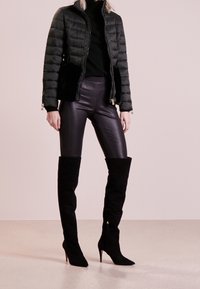 Czarna kurtka puchowa z akcentami z futra syntetycznego, dopasowane skórzane spodnie i wysokie czarne zamszowe szpilki. Gładka tekstura, smukły krój.