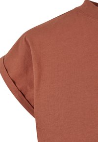 T-shirt en coton couleur rouille à manches courtes, montrant l'épaule et le détail du revers retroussé.