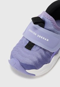 Chaussure de sport violette avec tige en maille, sangle ajustable et semelle en caoutchouc. Comprend des accents cousus et un capuchon de orteil texturé.