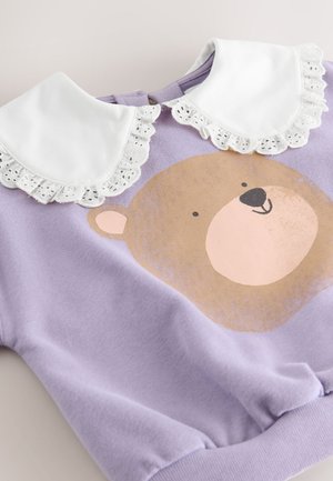 Lilla sweatshirt med bjørnegrafik, hvid krave med blonder og ribstrikkede manchetter, lavet af blødt stof med en glat tekstur.