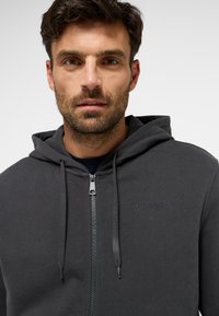 Sötétszürke cipzáras kapucnis sweatshirt, pamut keverékből készült, elöl cipzárral, állítható fűzőkkel és hímzett logóval a mellkason.