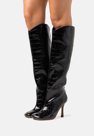 Czarne, lakierowane, wysokie botki do kolan z teksturą krokodyla, w szpic, z wysokim obcasem w stiletto, które wydłużają sylwetkę.