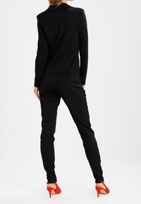Conjunto de americana y pantalones negros, con un corte ajustado y textura suave. Complementado con unos zapatos de tacón rojo.
