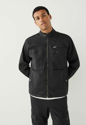 Schwarze Jacke mit hohem Kragen, zwei vorderen Reißverschluss-Taschen und einer glatten Textur. Verfügt über einen zentralen Reißverschluss und einen lässigen Schnitt.