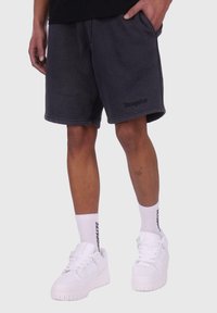 Grå bomulds shorts med afslappet pasform og sidelommer, med en foldet kant og diskret branding, da de er parret med hvide sneakers og sokker.