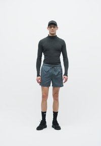 Completo sportivo caratterizzato da una maglietta aderente nera a maniche lunghe, pantaloni corti grigi, scarpe da ginnastica nere e un cappellino coordinato su uno sfondo bianco.