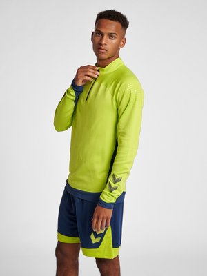 Langærmet, høj- synlighed limegrøn atletisk top med blå detaljer; parret med marineblå shorts med limegrønne detaljer og mønster.