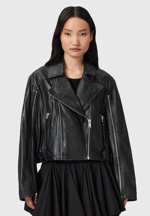 Giacca biker cropped in pelle nera con cerniere argentate, colletto ampio e tasche laterali. Presenta un design strutturato e una texture liscia.