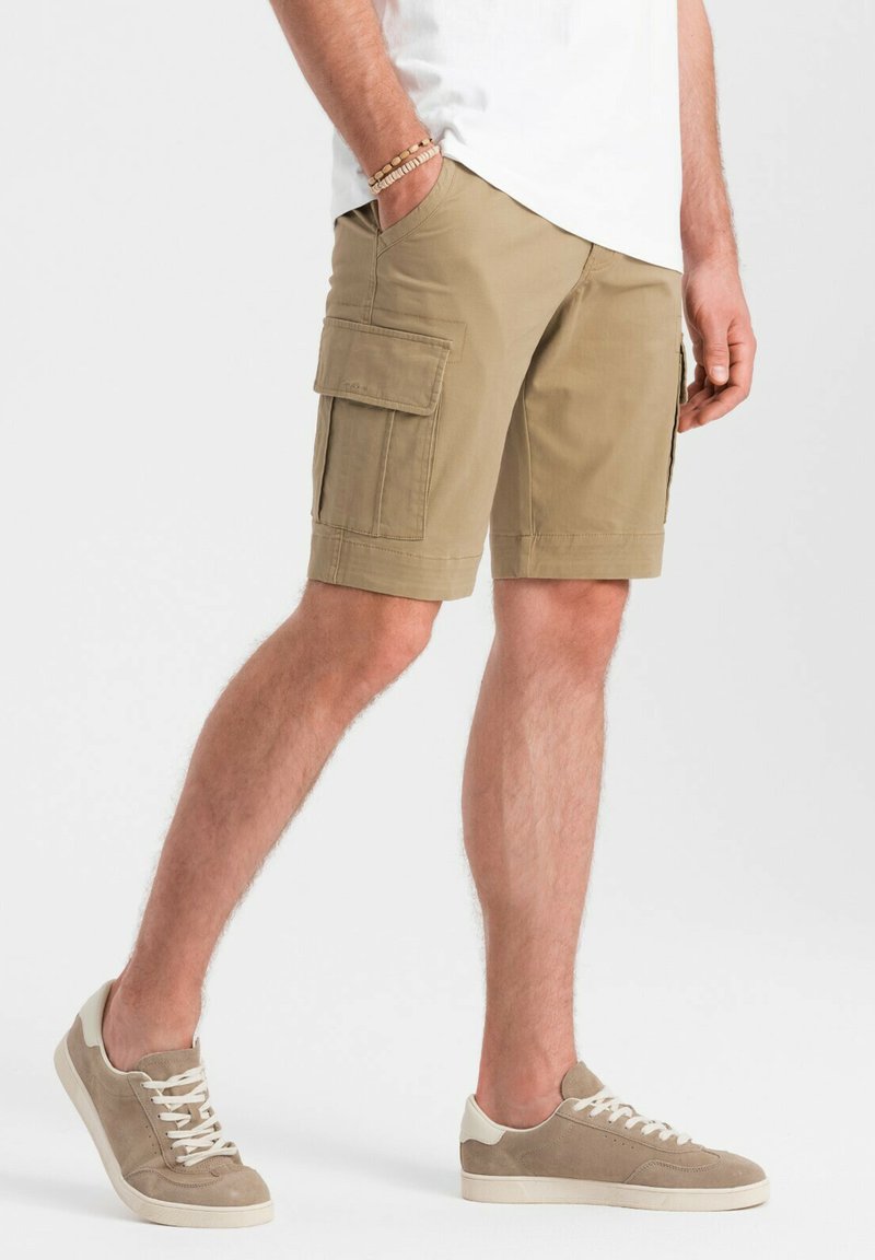 Pantaloni cargo khaki con tasche laterali, realizzati in tessuto leggero. Abbinati a sneakers in tela beige chiaro con lacci. Design semplice e pratico.