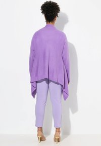 Cardigan in magenta a maglia aperta con orlo drappeggiato, abbinato a pantaloni leggeri color lavanda. Scarpe trasparenti con tacco alto completano l'outfit.